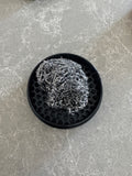 Metal scrubber resting on a black honeycomb-patterned dish on a gray marble countertop