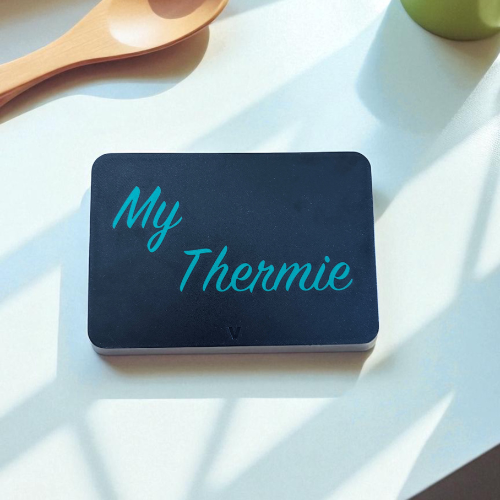 Black box with 'My Thermie' text on a white surface with a wooden spoon and green container in the background. TM7  display cover