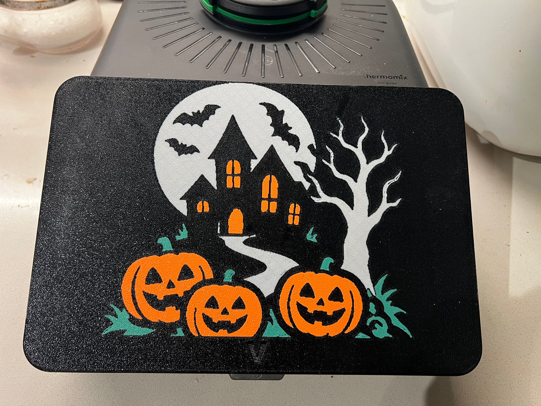 Haunted house Halloween screen cover on a Thermomix TM7 — full moon, crooked house with glowing orange windows, bats, bare tree and three jack-o'-lanterns