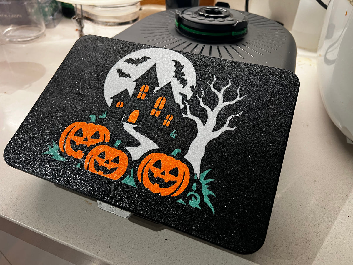 Haunted house Halloween screen cover on a Thermomix TM7 — full moon, crooked house with glowing orange windows, bats, bare tree and three jack-o'-lanterns