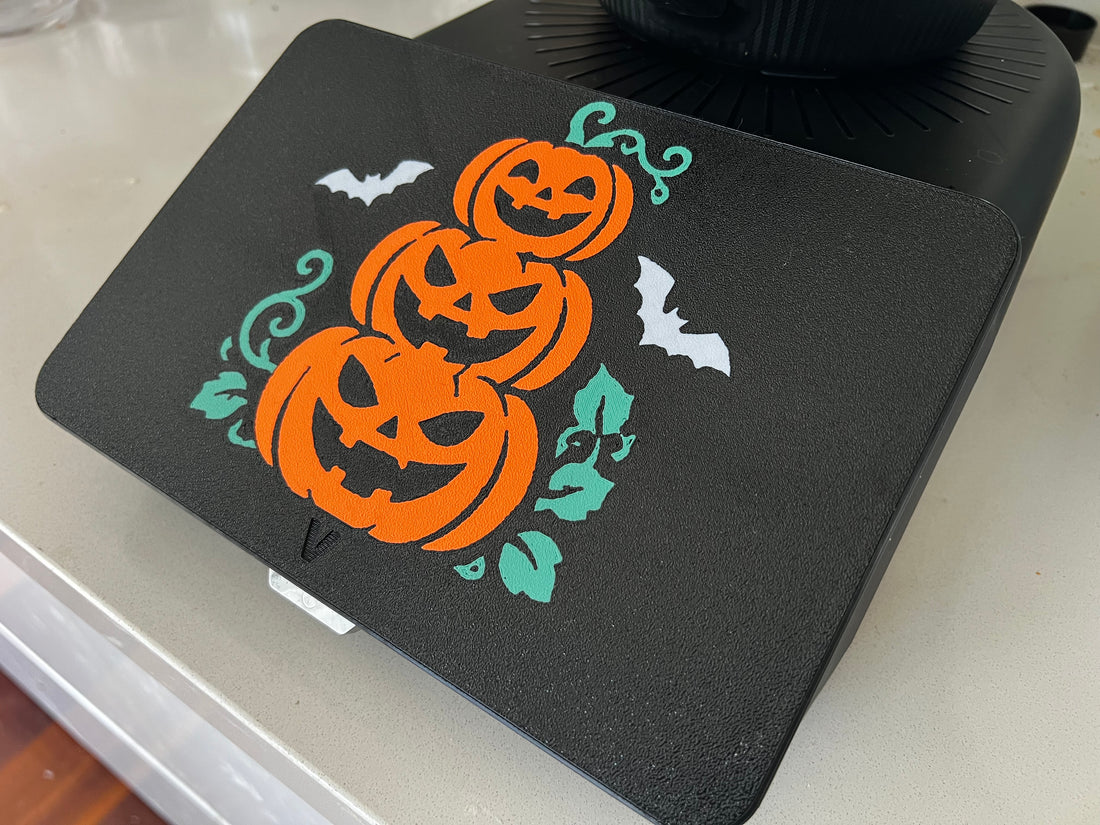 Pumpkin stack Halloween screen cover on a Thermomix TM7 — three orange jack-o'-lanterns with white bats and teal vines on black