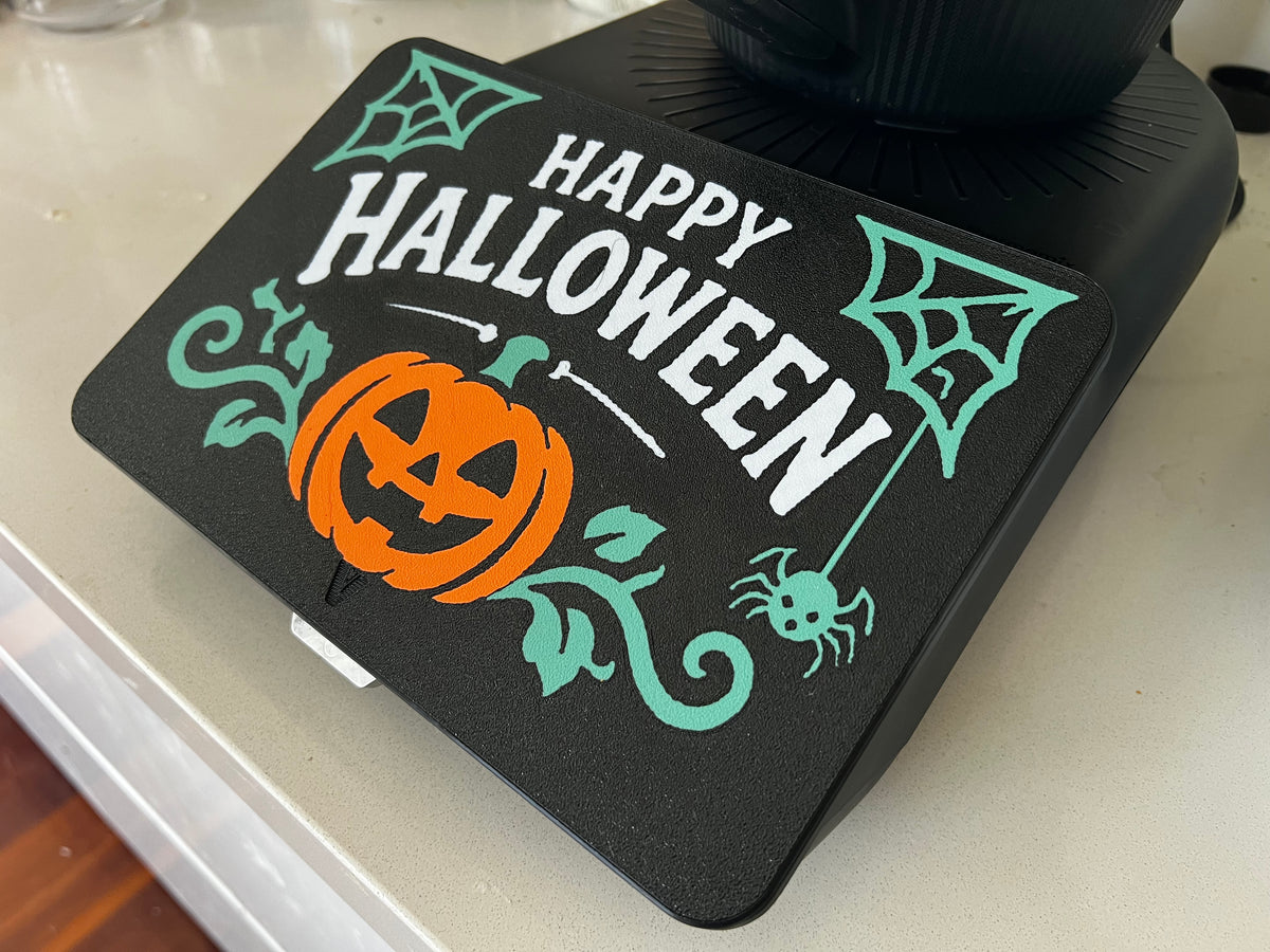Happy Halloween spider web screen cover on a Thermomix TM7 — white lettering with teal webs, vines and a spider on black